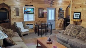 Un intérieur de chalet chaleureux, avec un revêtement mural en bois, un téléviseur, une table à manger avec des chaises et un canapé.