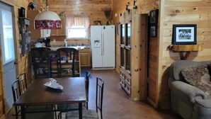 L’intérieur d’un chalet en bois comprend une table à manger, des chaises, un réfrigérateur et un canapé.