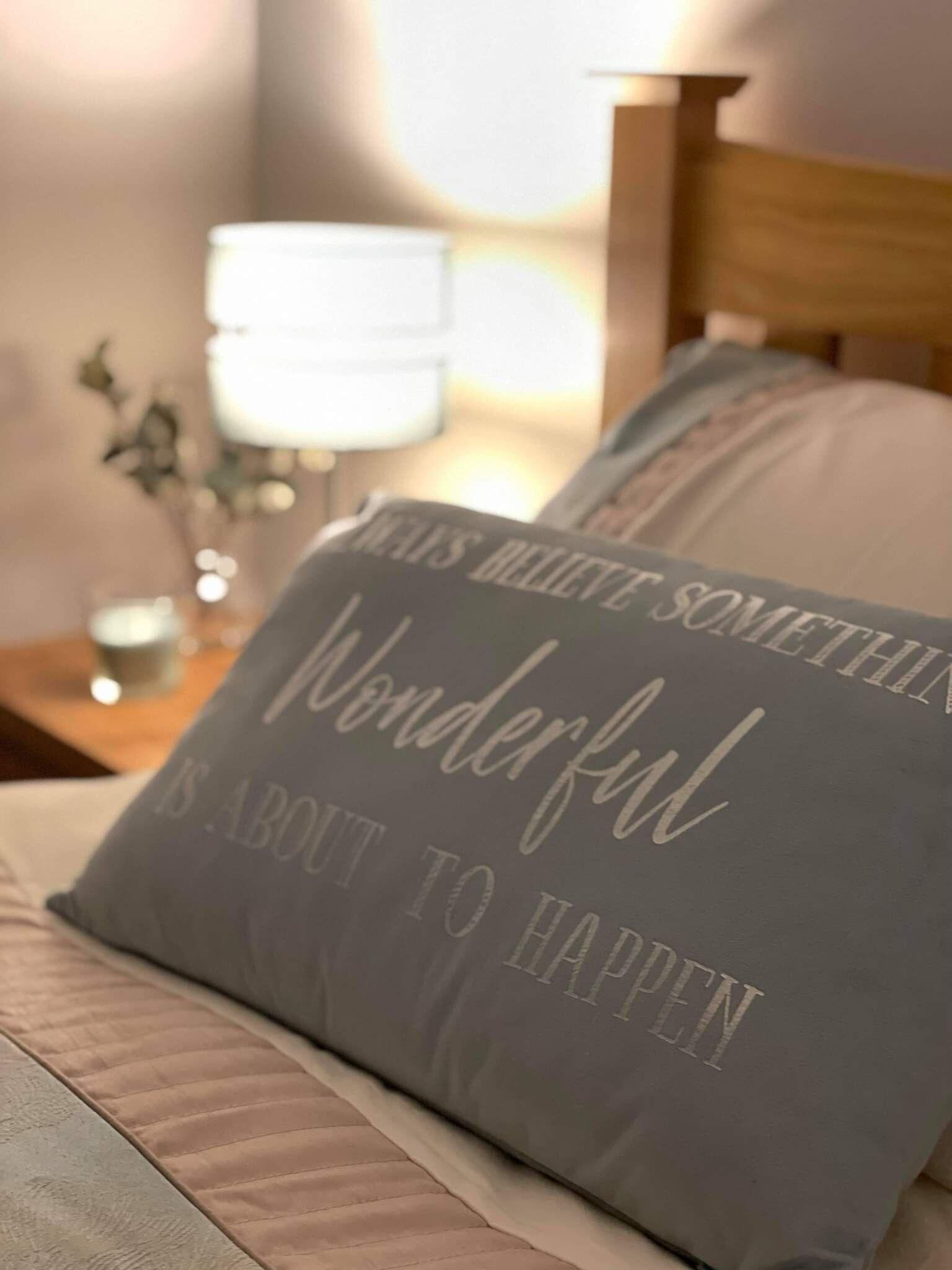A bed with a pillow that reads "WONDERFUL IS ABOUT TO HAPPEN".