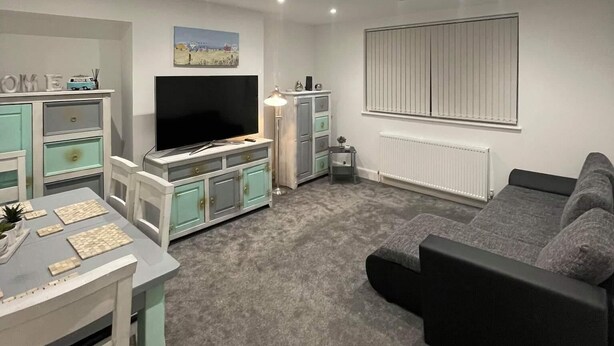 A modern living room with a grey sofa, a TV on a cabinet, a small table with a lamp, and a radiator.