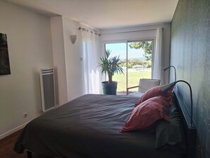 A bedroom with a bed, a potted plant, a window with curtains, and a view of the outdoors.