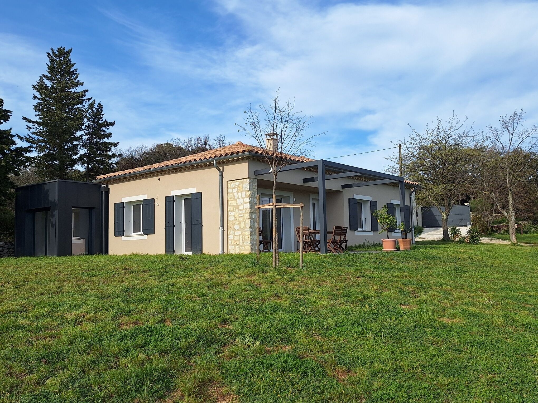 A modern house with a tiled roof, a stone wall, and a covered patio area.