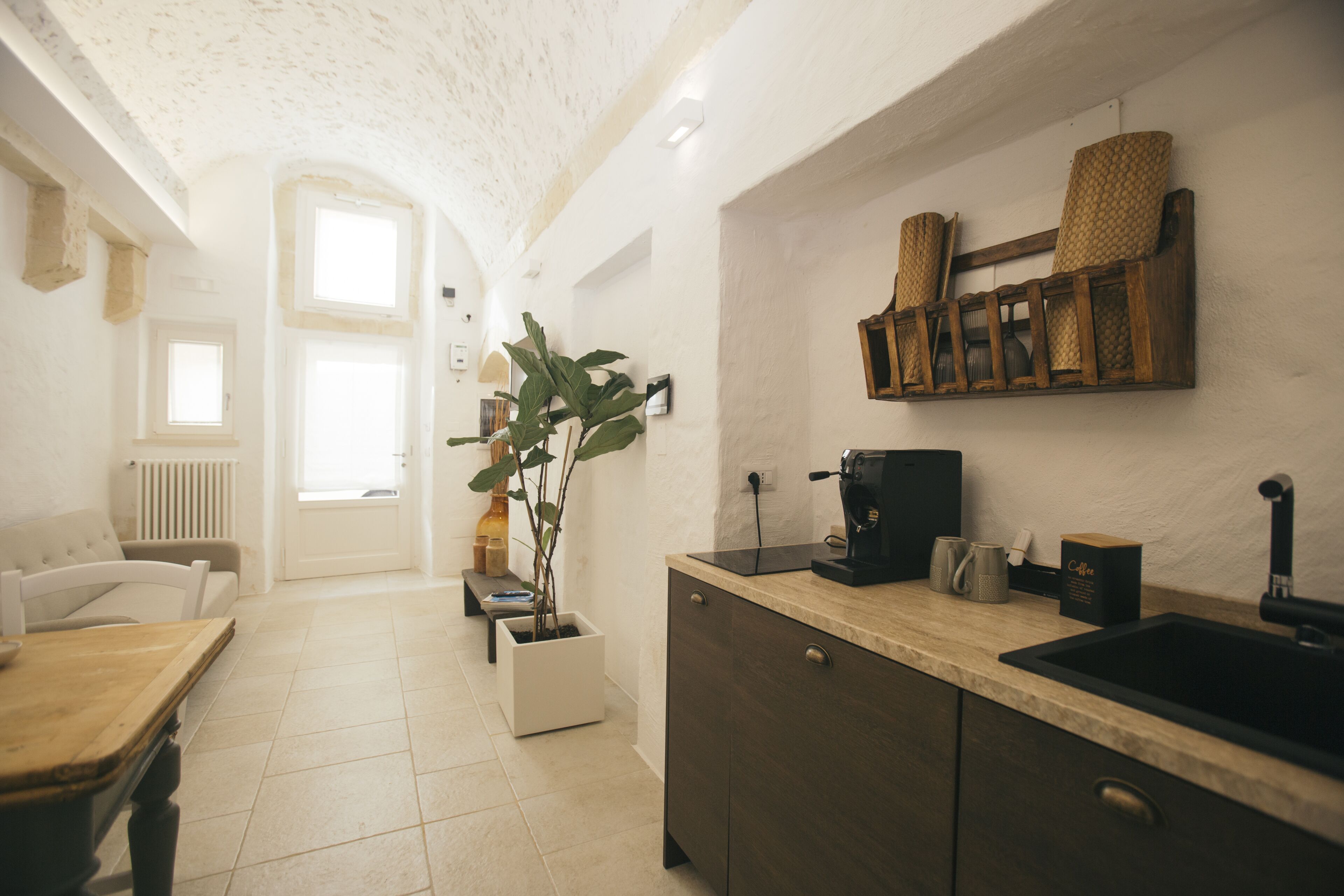 A kitchen with a wooden countertop, a coffee machine, and a sink. There is a potted plant and a white cabinet.