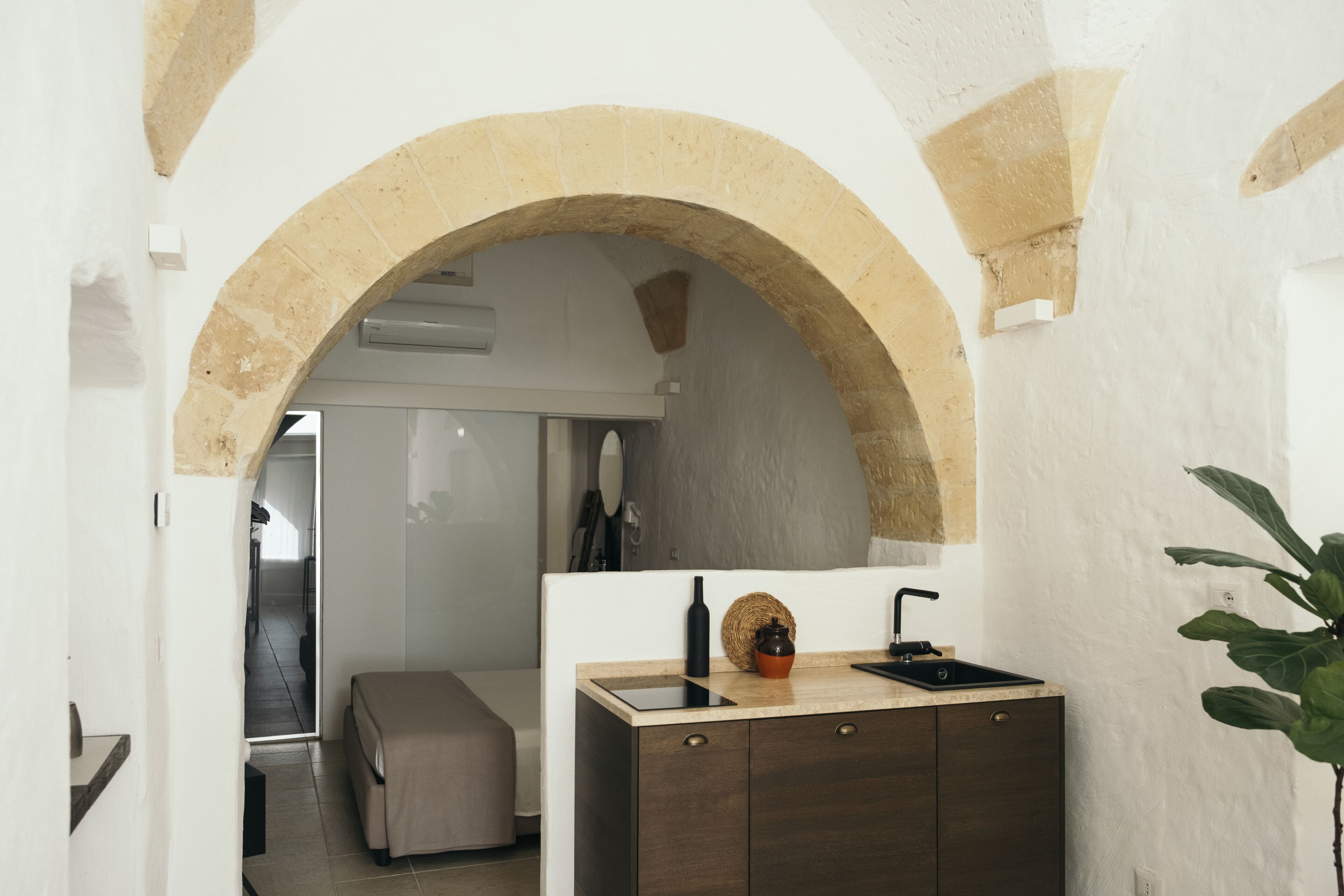 A compact kitchen with a stone archway, a countertop with a sink, and a small cabinet.