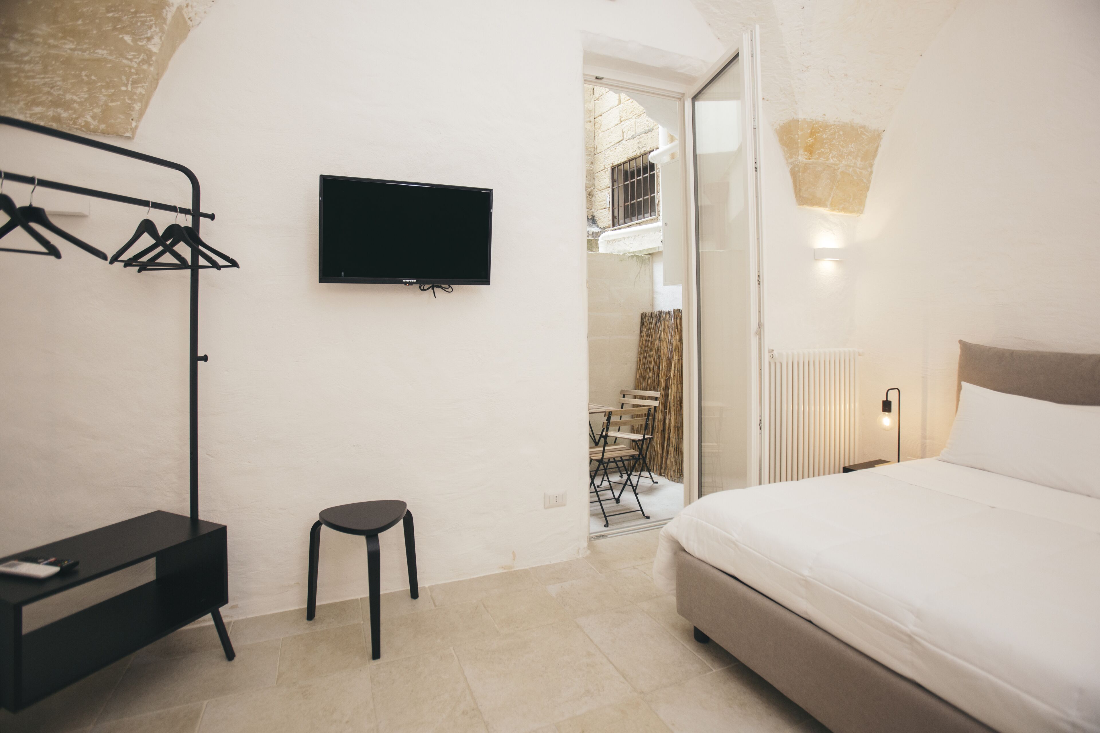 Un dormitorio con cama, televisor, perchero y un taburete pequeño.