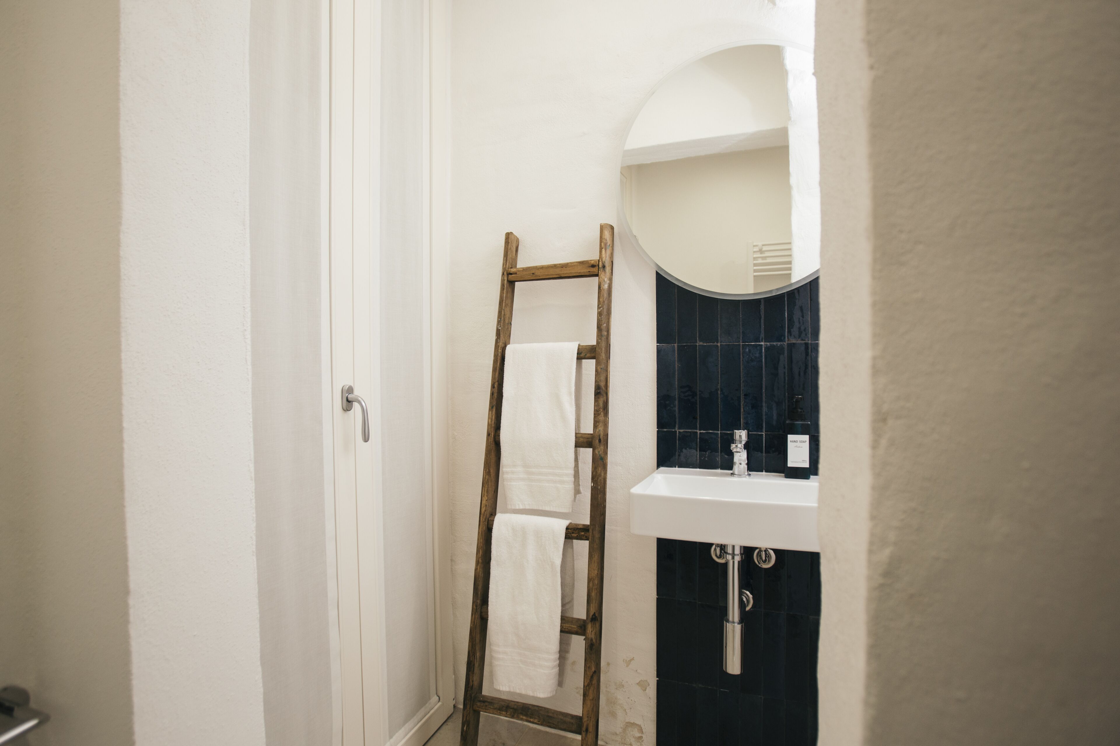 Un baño con una escalera de madera apoyada en la pared, un lavamanos blanco y una pared de azulejos oscuros.