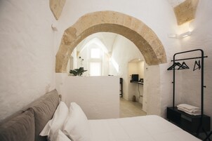 Un dormitorio con cama, perchero y vista a un baño a través de un arco.