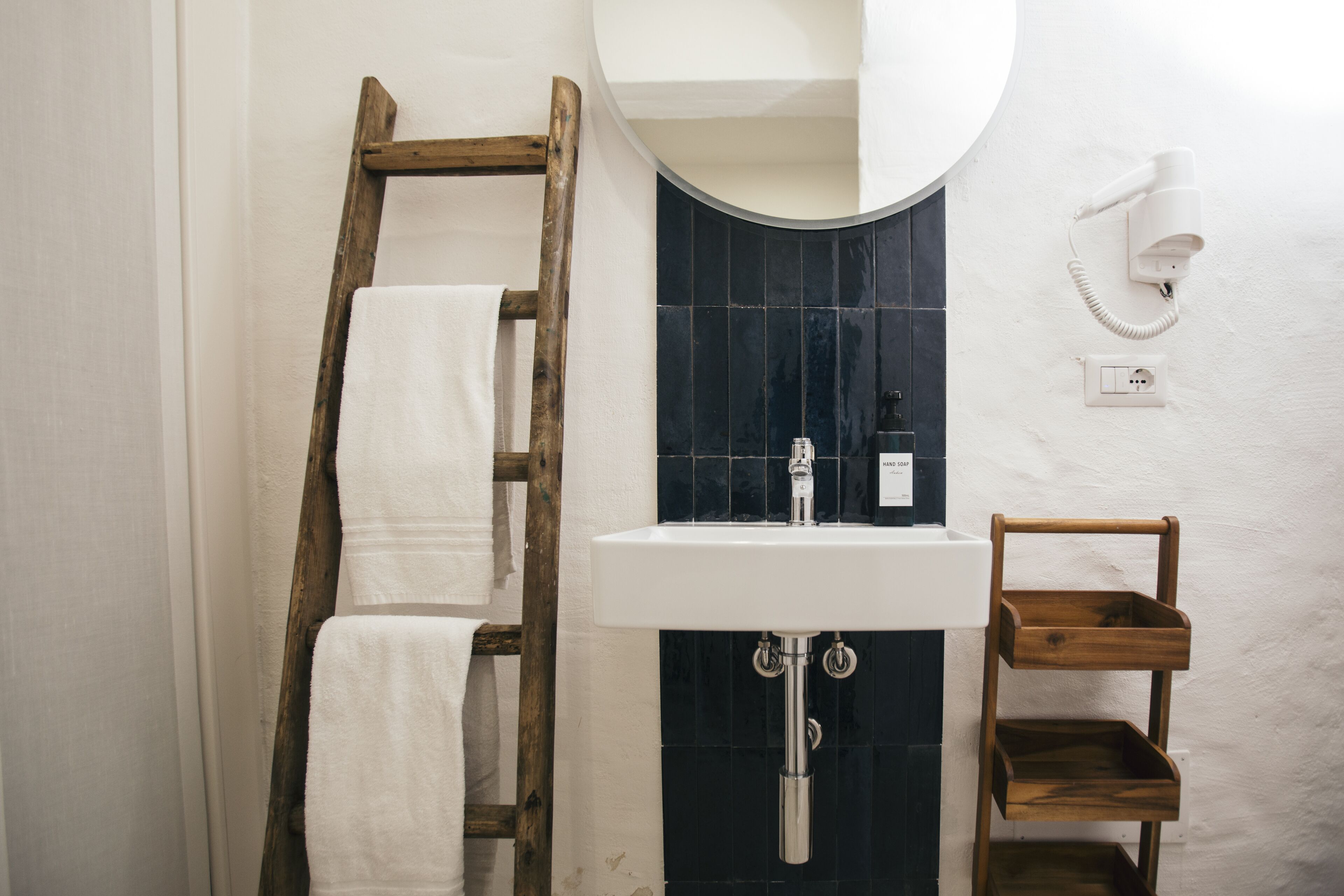 A bathroom with a wooden ladder, a white sink, and a wooden shelf.