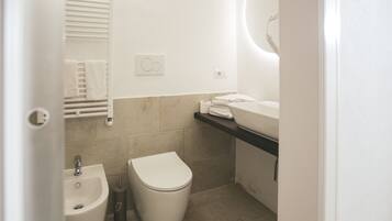Een moderne badkamer met een bidet, toilet, wastafel en handdoekhouder.