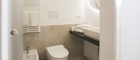 A modern bathroom with a bidet, toilet, sink, and towel rack.