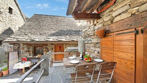 A stone building with a wooden door, a table set with plates, and chairs. - Rustico al Forno Sonogno Near Hiking Trails (Sonogno)