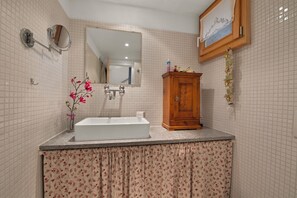A bathroom with a white sink, a wooden cabinet, a mirror, and a floral curtain.