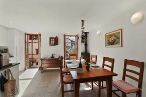 A dining area with a wooden table and chairs, a bench, and a view through an open door. - Rustico al Forno Sonogno (Sonogno)