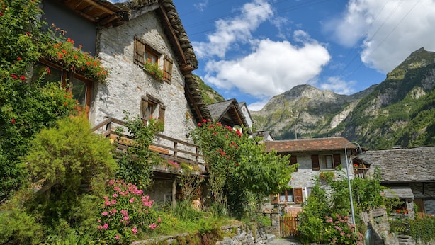A stone building with wooden shutters and flower boxes, surrounded by lush greenery and mountains in the background. - Rustico al Forno Sonogno Near Hiking Trails (Sonogno)