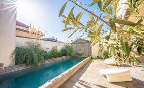 Une piscine bordée de pierres, entourée de verdure et adossée à un petit bâtiment.