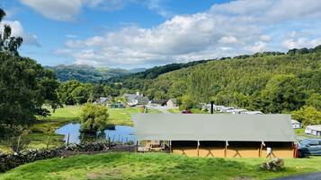 Paisagem rural com uma grande estrutura em forma de tenda, um lago e uma estrada.