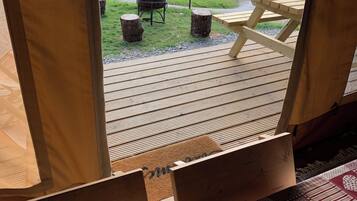 A view from inside a cabin with a wooden deck, a picnic table, and a doormat with a heart pattern.