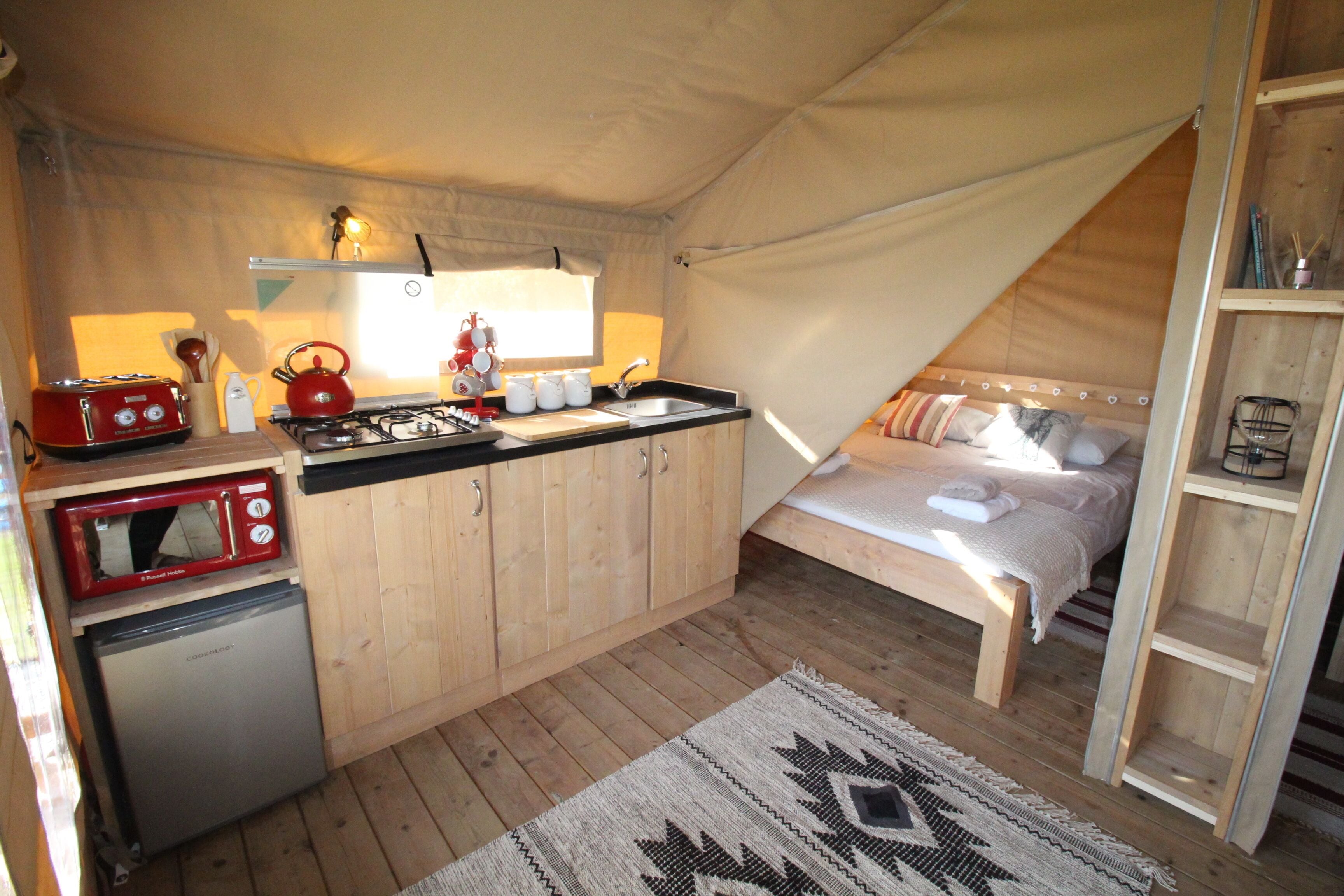 A compact tented accommodation with a kitchenette, a bed, and a small refrigerator.