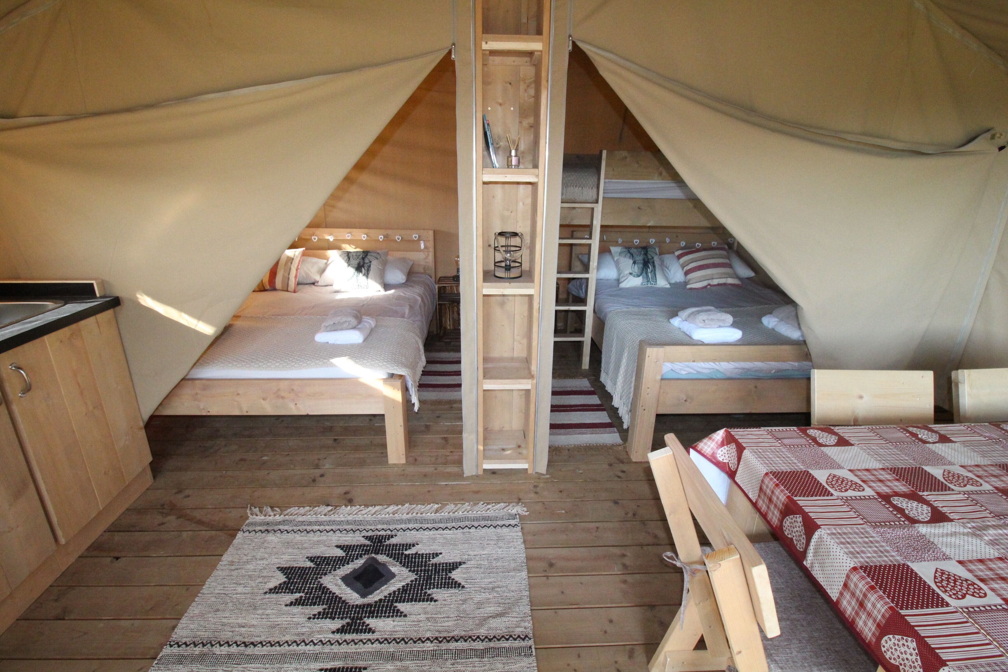 Una carpa con dos camas, una escalera de madera y una pequeña zona de cocina.