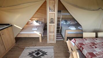 Una carpa con dos camas, una escalera de madera y una pequeña zona de cocina.
