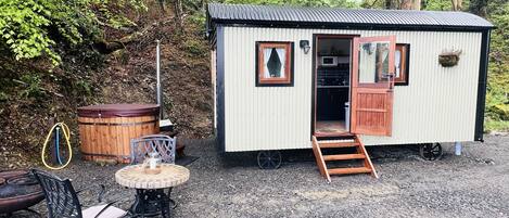 A small cabin with a wooden deck, a metal roof, and a kitchen visible through the open door.