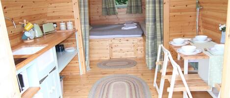 A compact wooden cabin with a kitchenette, a small sleeping area, and a bathroom.