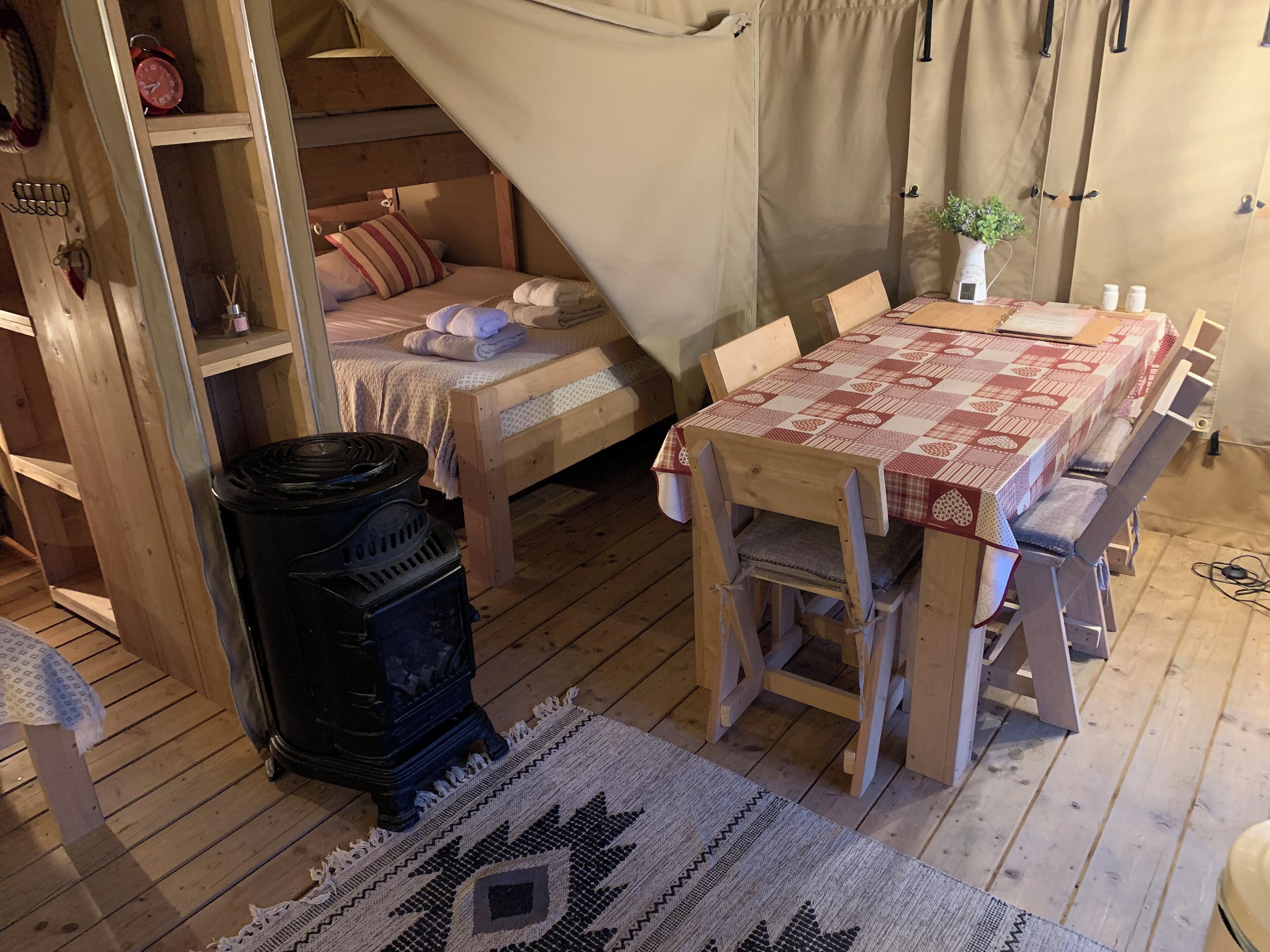 L’intérieur chaleureux d’un chalet avec un lit en bois, une table recouverte d’une nappe à carreaux, un poêle à bois et une décoration rustique.