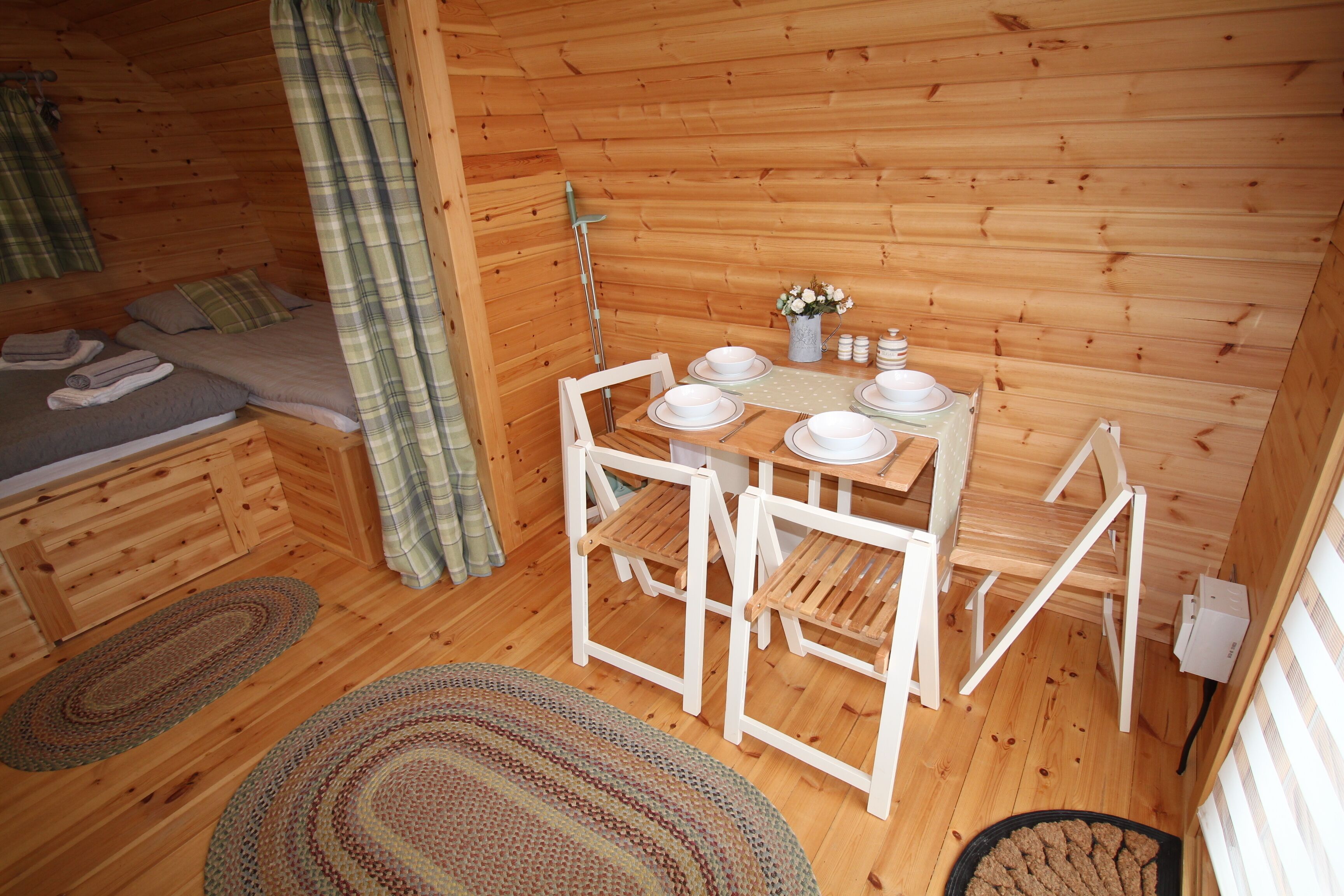 A cozy cabin with a wooden interior, a dining table set with plates and cutlery, and a bed with neatly folded towels.
