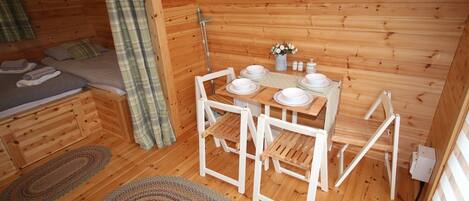 A cozy cabin with a wooden interior, a dining table set with plates and cutlery, and a bed with neatly folded towels.