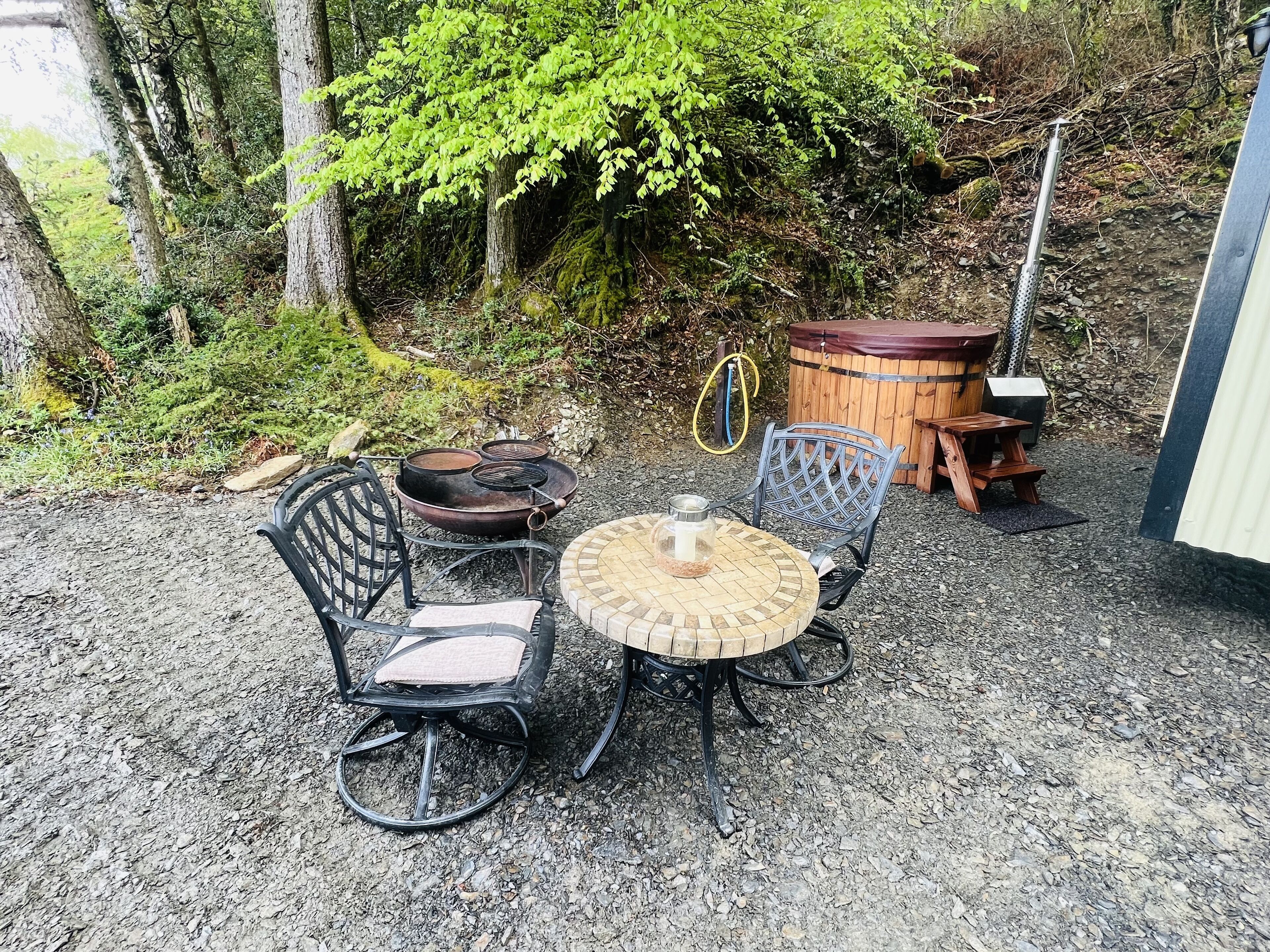 An outdoor seating area with a round table and chairs, a wooden barrel, and a metal chair with a cushion.
