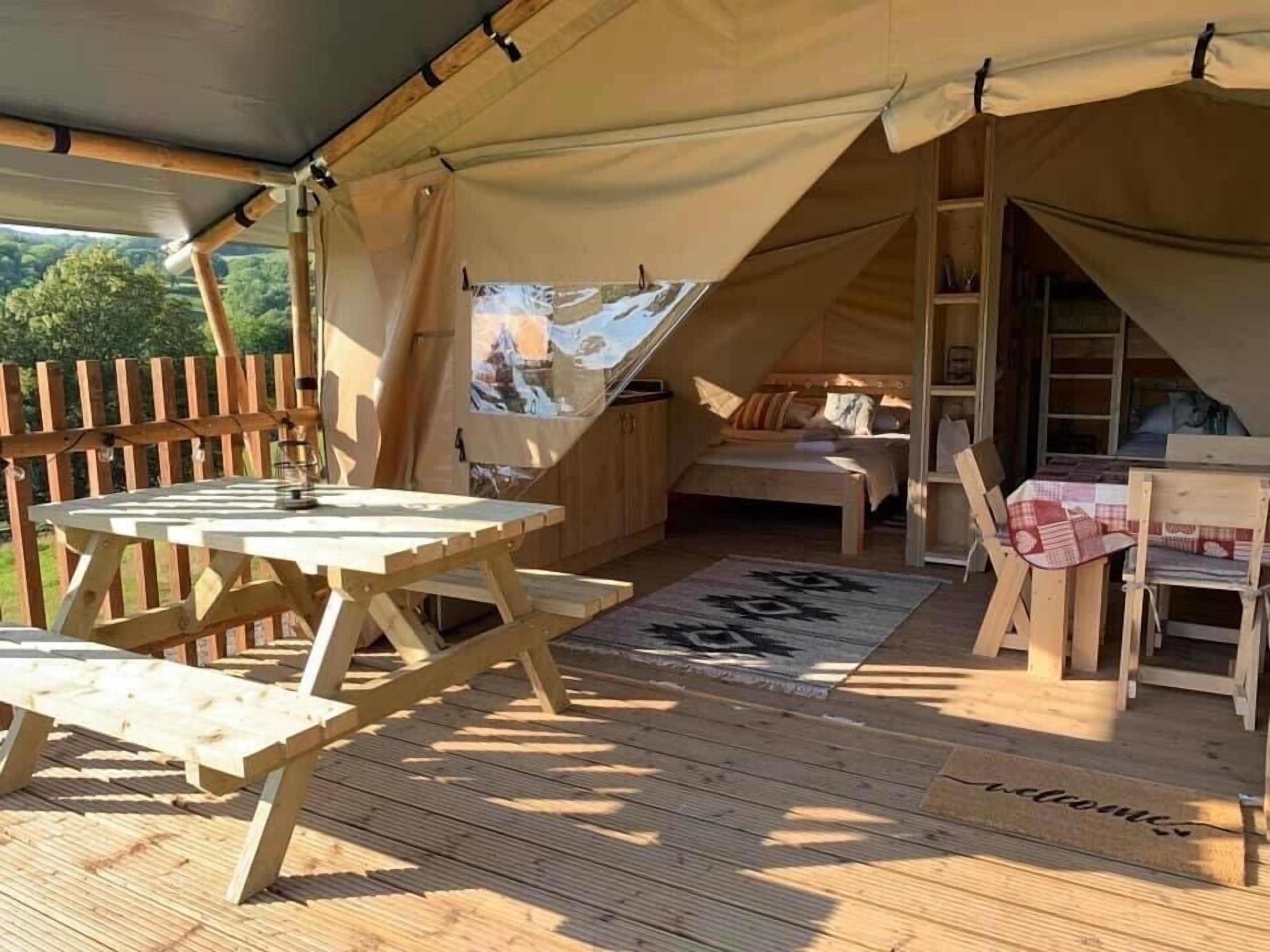 A cozy tented accommodation with a wooden deck, a small bed, and a table with chairs.