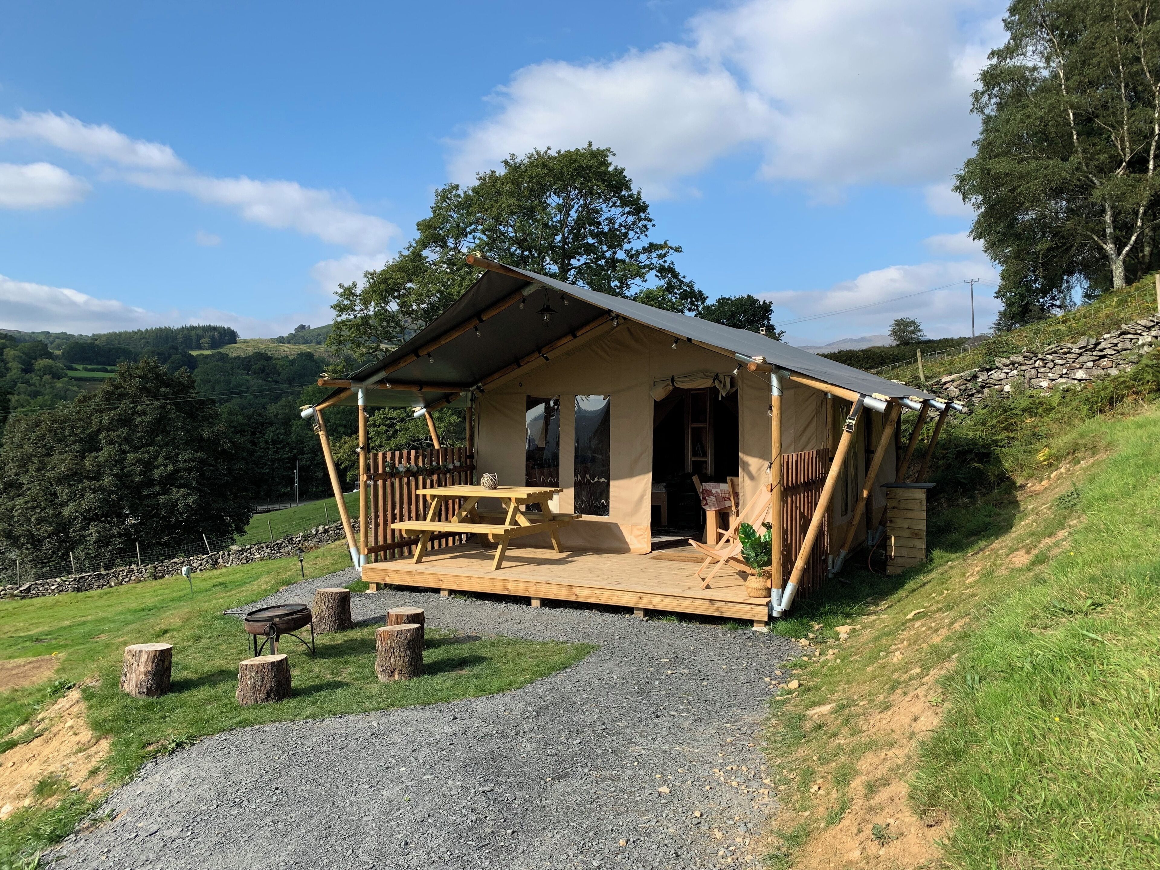 Eine rustikale Holzhütte mit einer Holzterrasse, einem Picknicktisch und einer Steinmauer im Hintergrund.