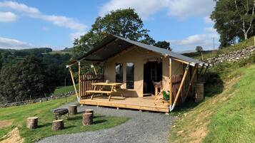 Eine rustikale Holzhütte mit einer Holzterrasse, einem Picknicktisch und einer Steinmauer im Hintergrund.