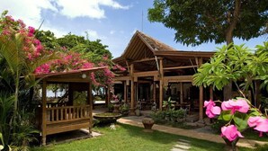A wooden gazebo with a thatched roof, surrounded by lush greenery and pink bougainvillea flowers. - Pondok Sari Beach & Spa Resort (Pemuteran)