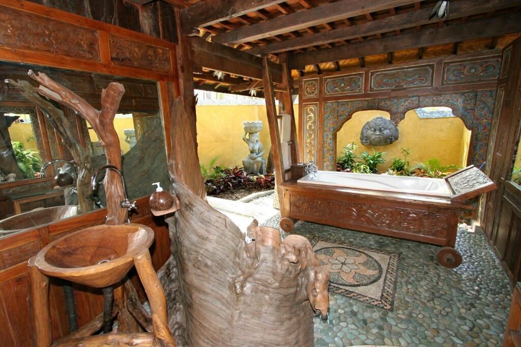 A rustic bathroom with a wooden basin, a large tree trunk sculpture, and a stone bench.