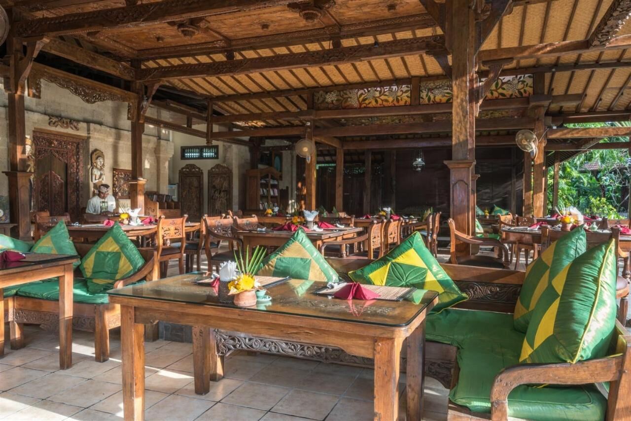 Un espace de restauration intérieur avec des meubles en bois et un décor traditionnel. Les tables sont agrémentées de coussins verts et jaunes.
