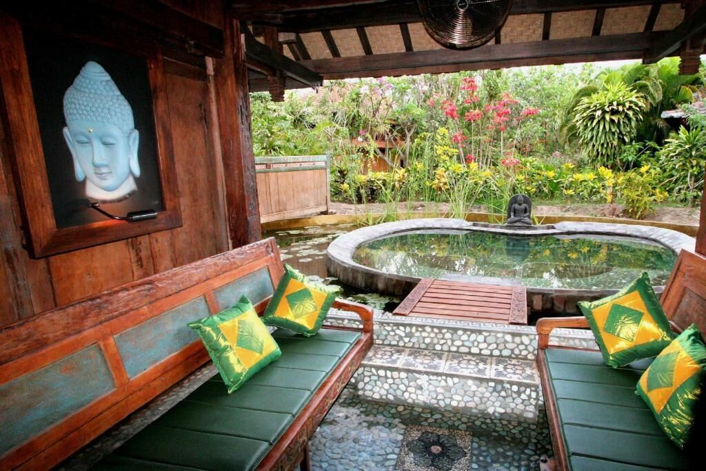A wooden deck with a Buddha statue, a hot tub, and a garden with various plants and flowers.