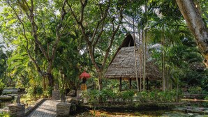 A thatched-roof hut with a stone pathway leading to it, surrounded by lush greenery and a small pond with lily pads. - Pondok Sari Beach & Spa Resort (Pemuteran)