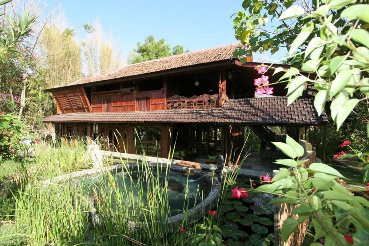 A traditional wooden house with a tiled roof, a wooden deck, and a small pond with water lilies.
