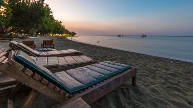 A beach with wooden lounge chairs and a bench, a calm sea, and a sunset in the background. - Pondok Sari Beach & Spa Resort (Pemuteran)