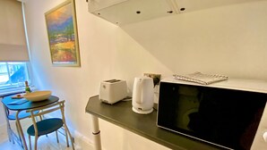 Une cuisine avec un plan de travail noir, un grille-pain, une bouilloire et un four à micro-ondes. Il y a une fenêtre donnant sur des arbres et un tableau accroché au mur.