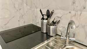 Une cuisine moderne dotée d’un évier en acier inoxydable, d’un plan de travail noir et d’un pare-feu en marbre.