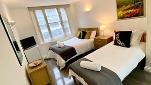 Une chambre d’hôtel avec deux lits, une télévision, une fenêtre et un tableau au mur.