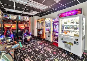 Une salle avec des jeux d’arcade, un sol orné de motifs en forme d’étoiles et un distributeur automatique proposant divers articles.