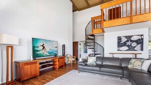 A spacious living room with a wooden entertainment unit, a large flat-screen TV, a leather sofa, and a staircase leading to an upper level.