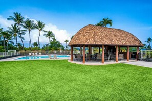 Un espace extérieur abrité, doté d’une piscine, et entouré de pelouse et de palmiers.