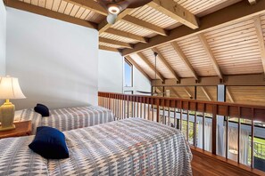 A bedroom with two beds, a nightstand, a lamp, and a balcony with a railing.