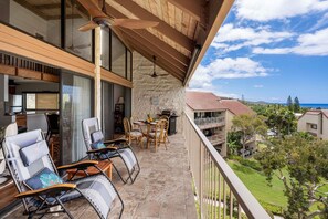 A balcony with outdoor seating, a stone wall, and a view of the ocean.