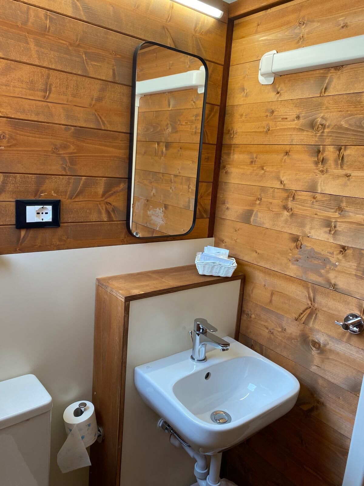 Une salle de bain avec des lambris en bois, un lavabo blanc, un miroir et des toilettes.