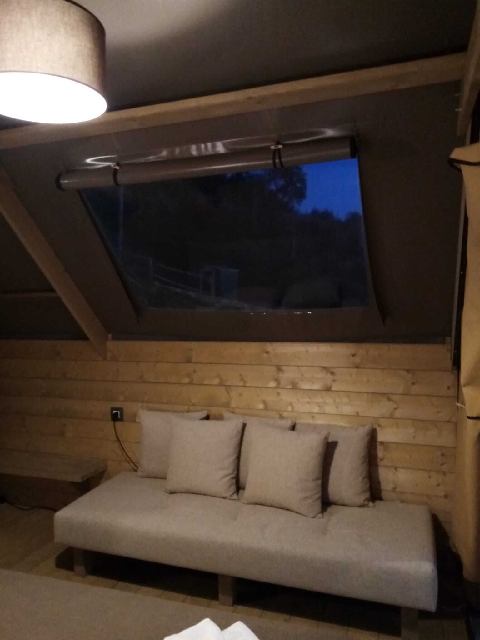 A cozy room with a sloped ceiling, a wooden wall, a window, and a sofa with cushions.